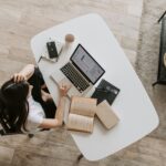 A woman working remotely on a laptop at home, analyzing data on screen, with books and a notebook on the table. Ideal for remote work and passive income topics.