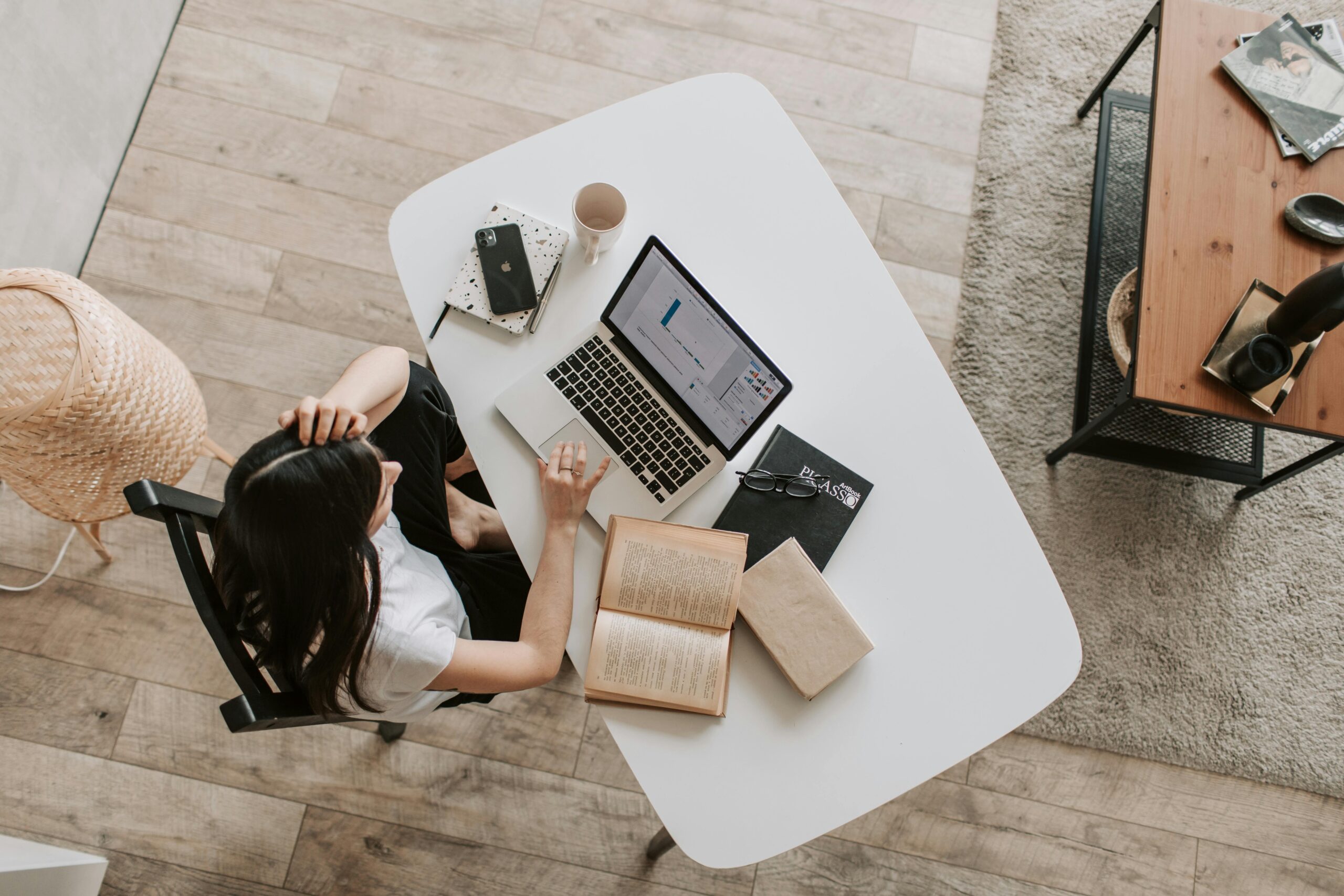 A woman working remotely on a laptop at home, analyzing data on screen, with books and a notebook on the table. Ideal for remote work and passive income topics.